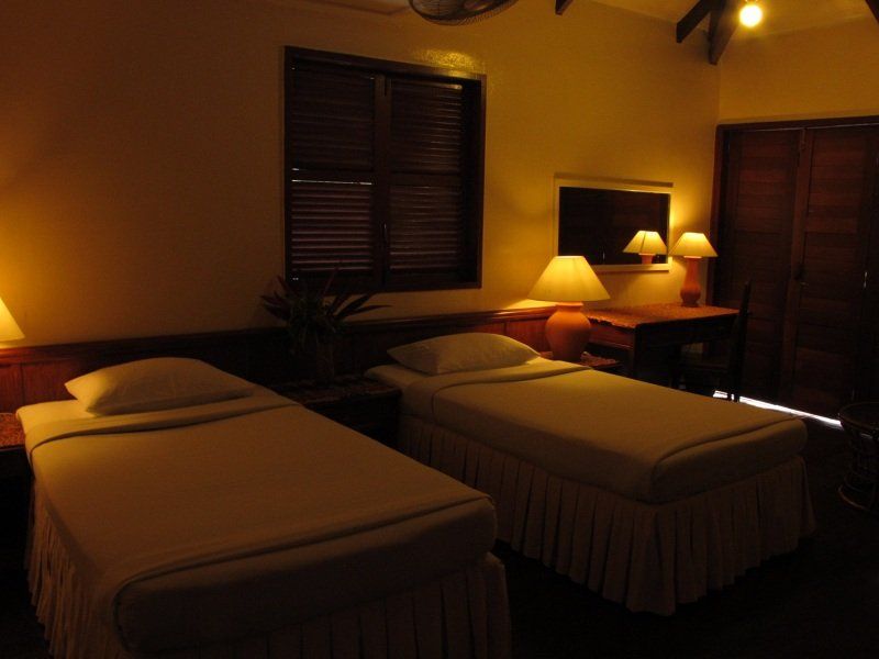 Two twin beds in a room with a desk, window, and warm lighting.