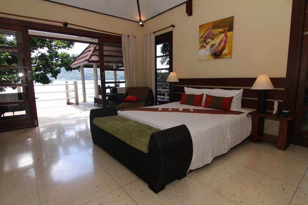 Bedroom with a bed, open doors to an outdoor area with a view of water and a small building.