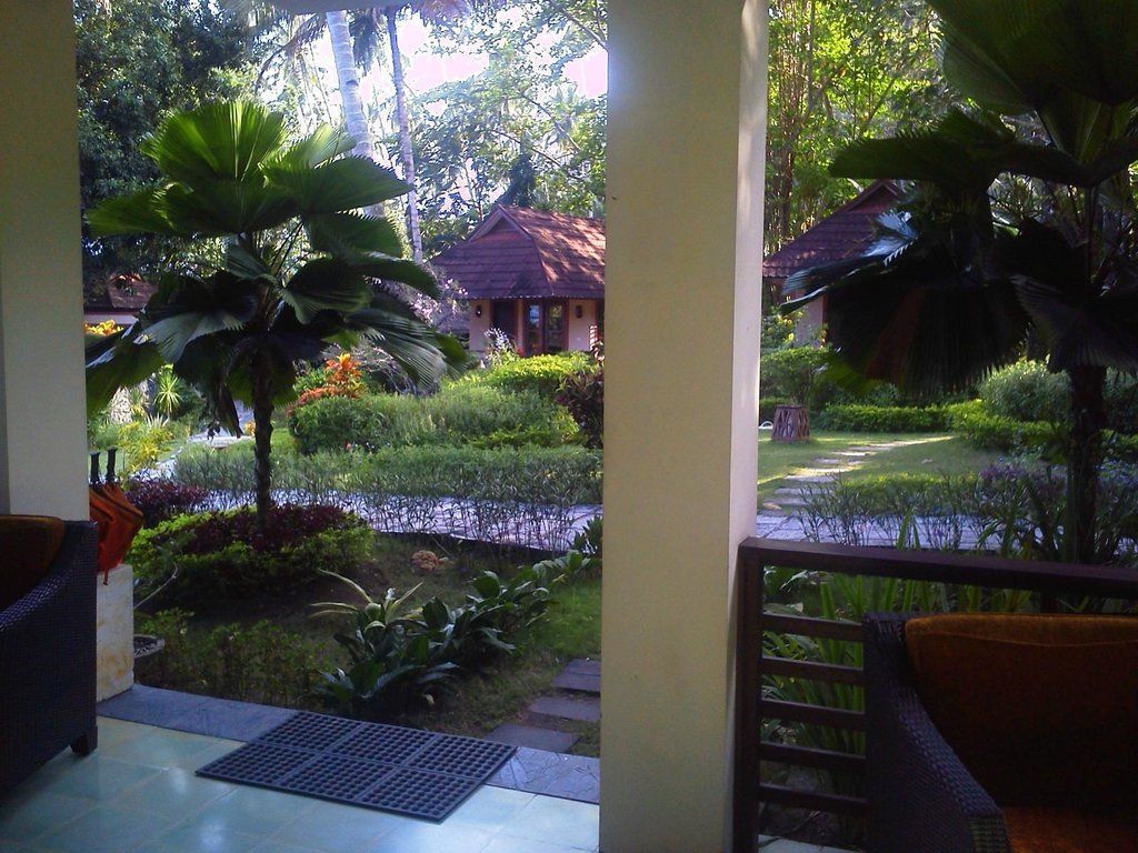 View of tropical garden from a porch with bungalow and trees.
