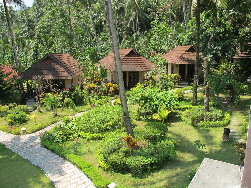 Villas with brown roofs and green gardens in a tropical resort setting.