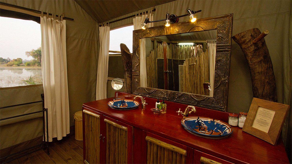 Bathroom in safari tent with red counter, large mirror, and view of water.