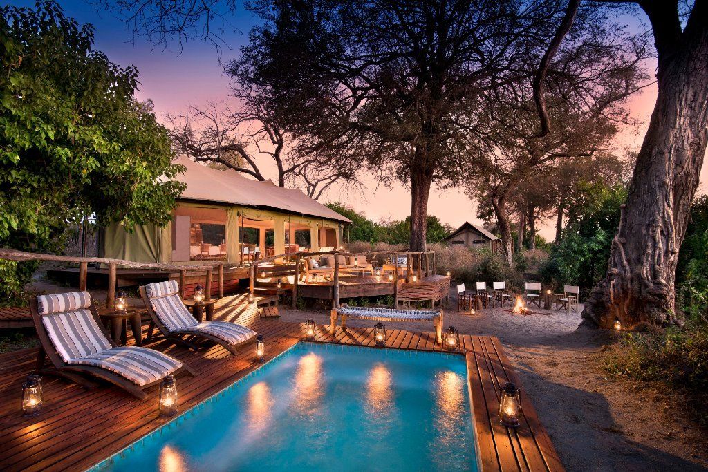 Poolside safari lodge at dusk with pool, lounge chairs, and lit lanterns.