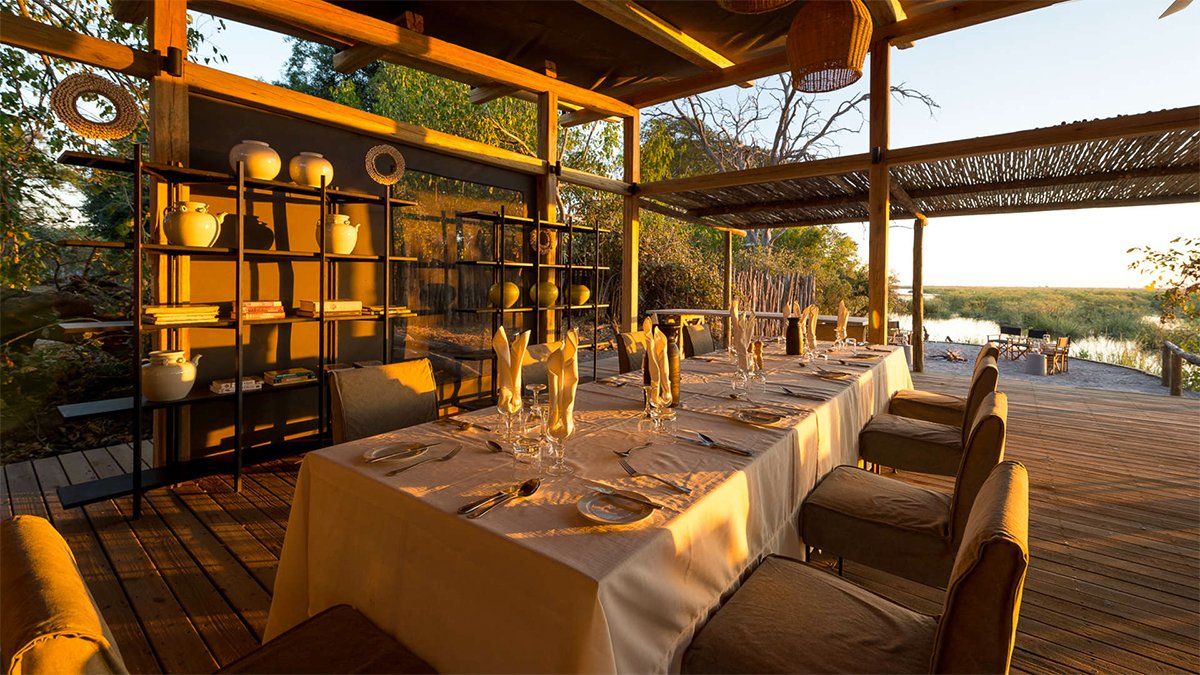 Outdoor dining table set for a meal on a wooden deck, overlooking a water view.