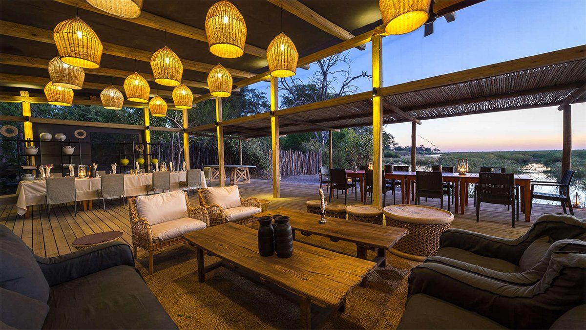 Outdoor lounge area with seating, tables, and decorative hanging lights. Dining tables set in the background with a dusk sky.