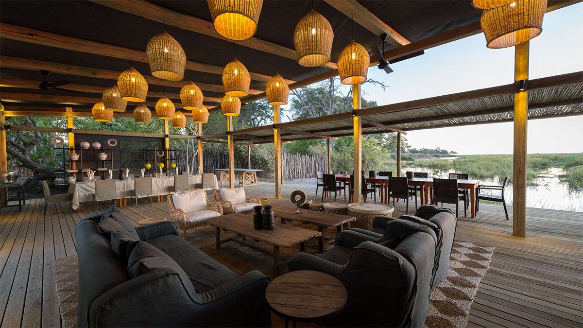 Open-air dining area with couches, tables, and woven pendant lights. Overlooks a marshy landscape.