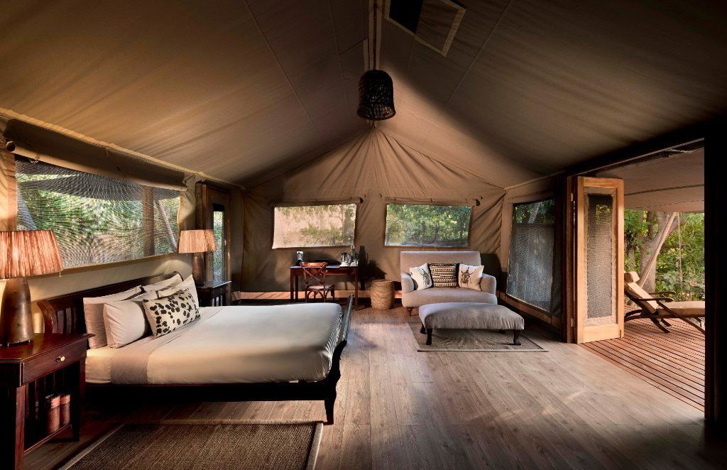 Spacious tent interior with bed, couch, and desk, open to a deck with trees.