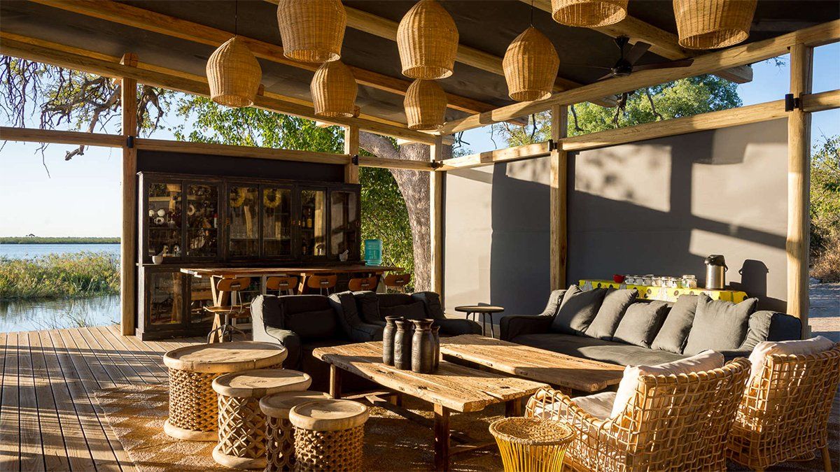Outdoor lounge with woven furniture, bar, and hanging basket lights by the water.