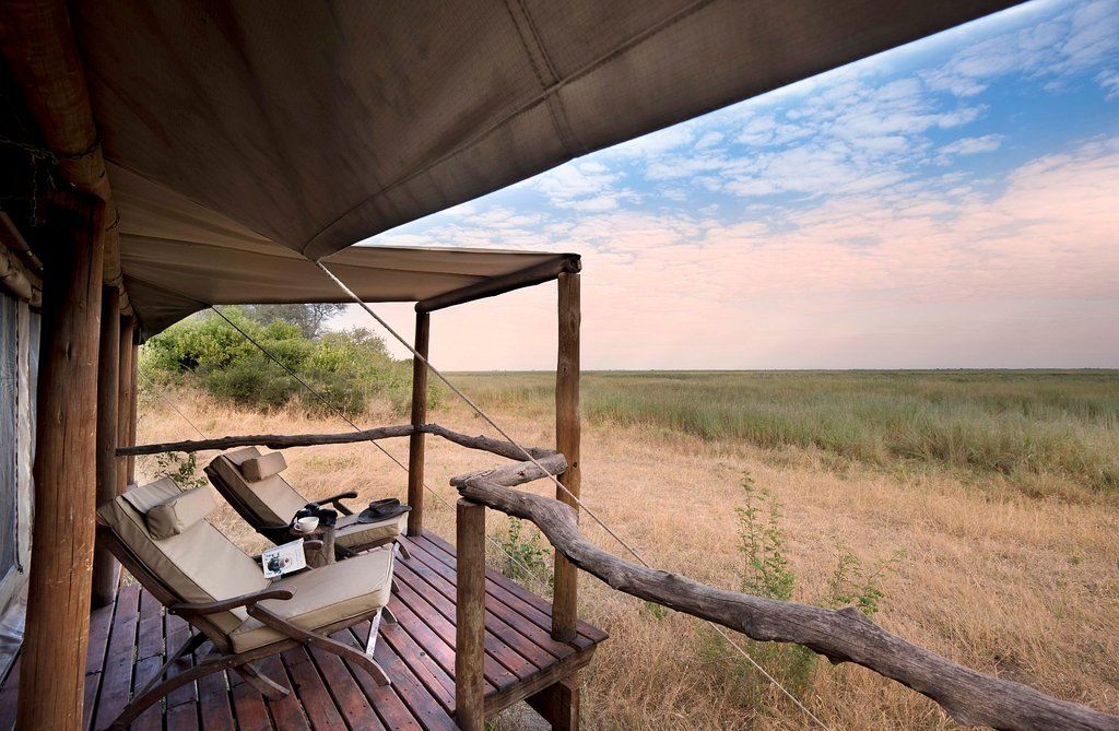 Wooden deck of safari tent with chairs, overlooking dry grassland and cloudy sky.