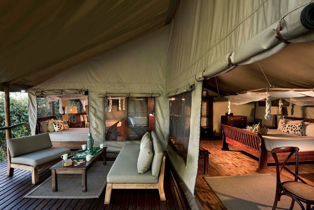 Canvas tent interior with seating area and bedroom, overlooking a natural landscape.