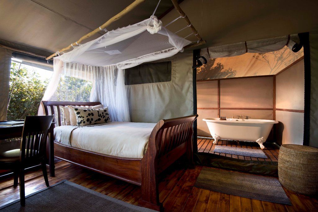 Luxury safari tent bedroom with a bed, desk, and freestanding bathtub.