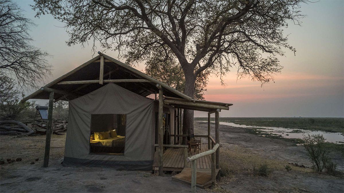 Safari tent with a porch near a waterway at dusk.