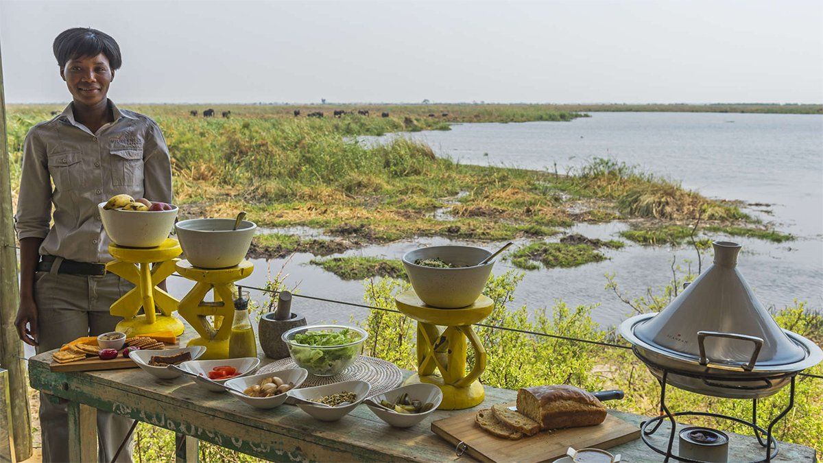 Woman by a lakeside buffet with bowls of food and a tagine.