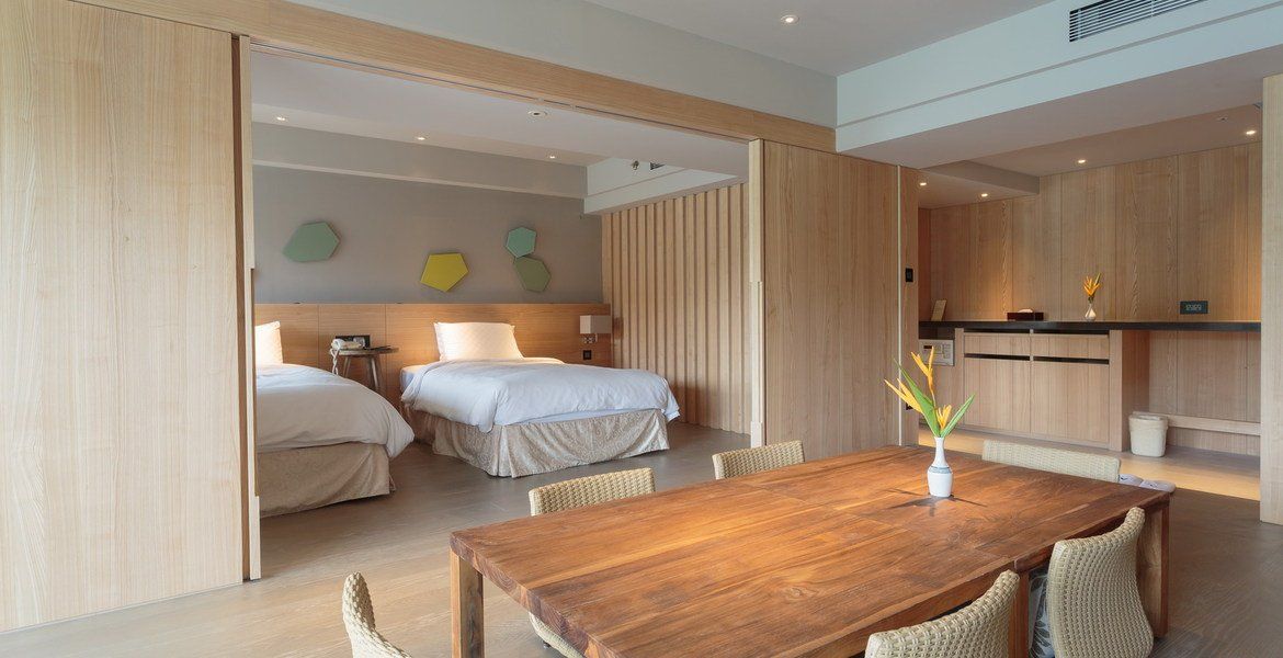 Hotel room with two beds, a dining table, and wooden walls.