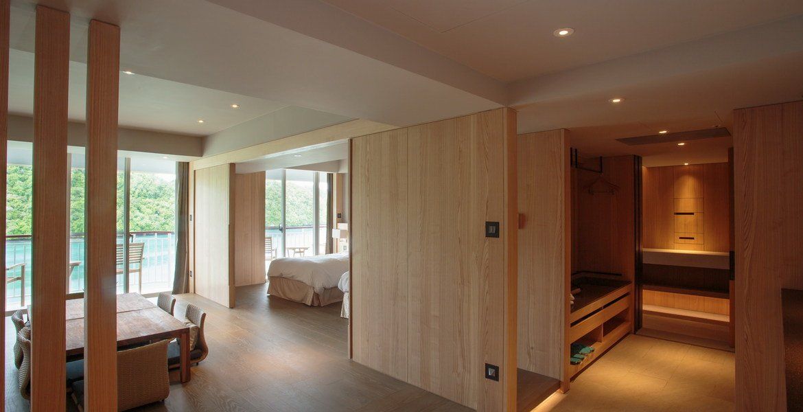 Interior view of a modern hotel suite with wooden paneling, dining area, and bedroom.