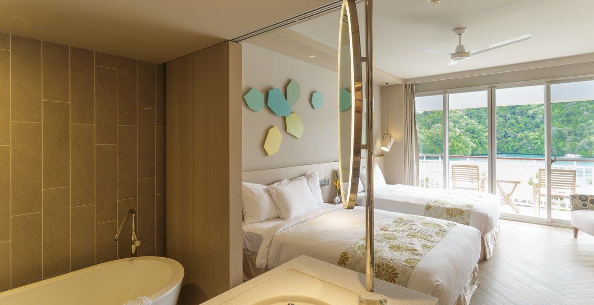 Hotel room with two beds, a freestanding bathtub, and a balcony overlooking water.