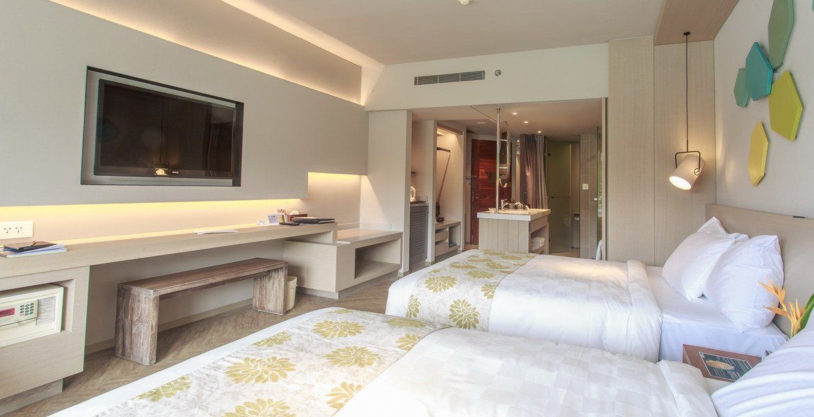 Modern hotel room with two twin beds, TV, desk, and bathroom visible.