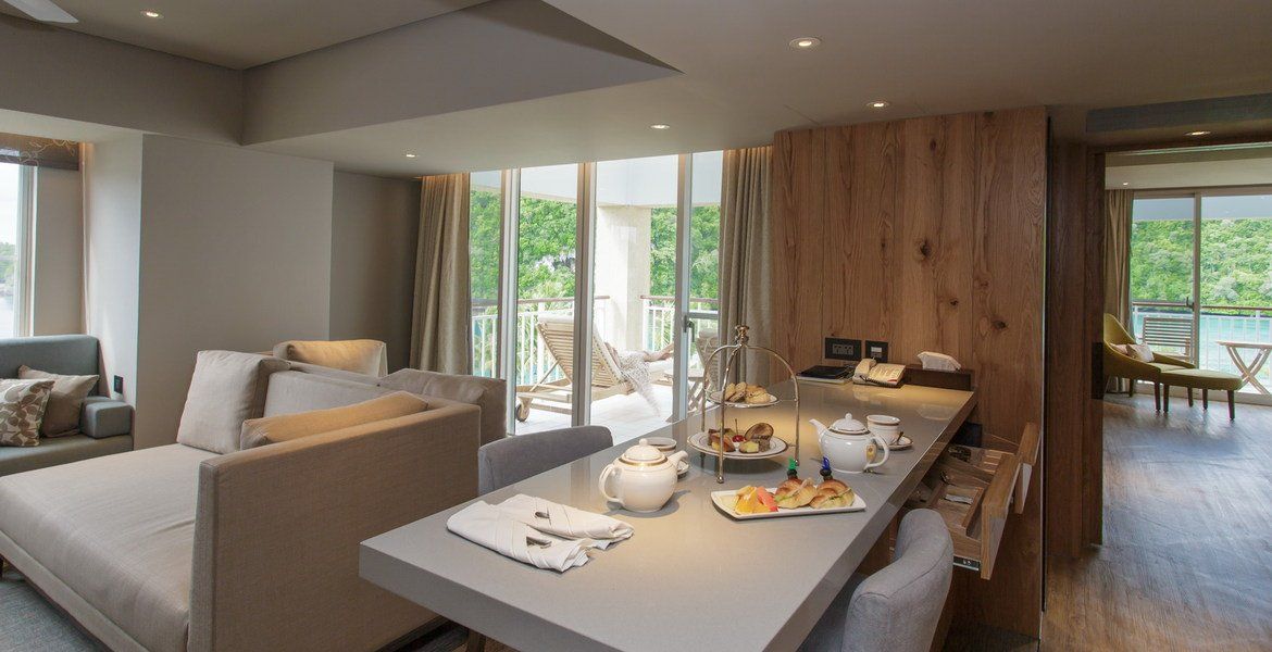 Luxury hotel suite with a breakfast bar, balcony, and lounge area, overlooking the ocean.