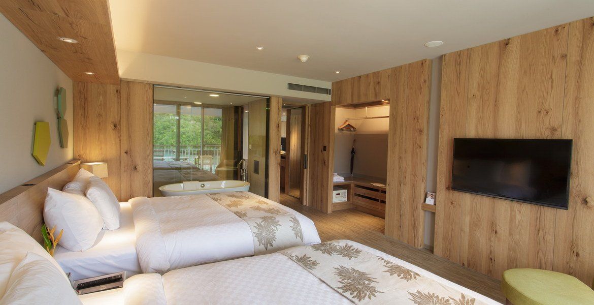 Hotel room with two beds, wood paneling, TV, and a view of a patio with a hot tub.