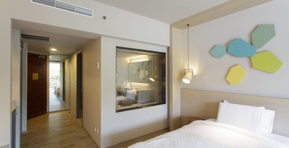 Hotel room interior with bed, bathroom view, hallway, and abstract wall art.