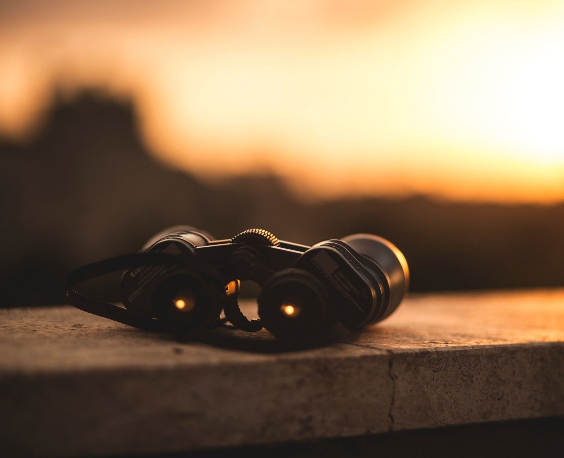 Binoculars on a stone surface, silhouetted against a golden sunset.