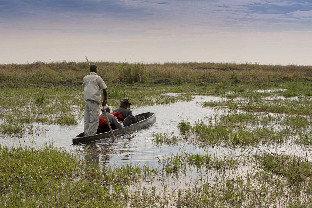 People in a canoe on a marsh, guided by a person standing at the back.