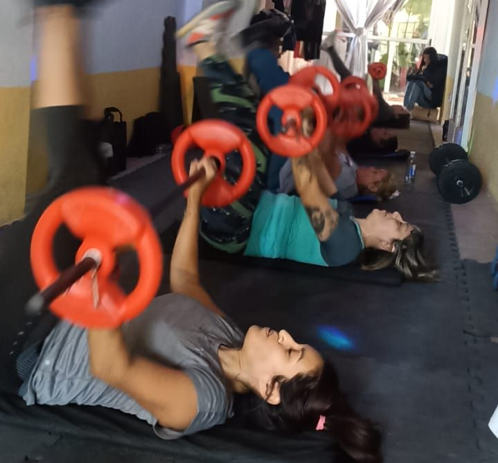 Personas levantando pesas en el gimnasio. Están tumbadas y sujetando mancuernas rojas por encima de la cabeza.