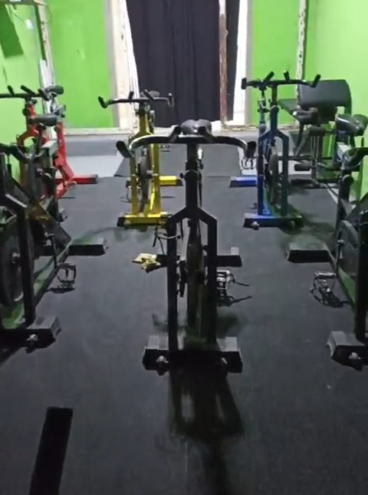 Bicicletas estáticas en un gimnasio bien iluminado, con paredes verdes y suelo oscuro.