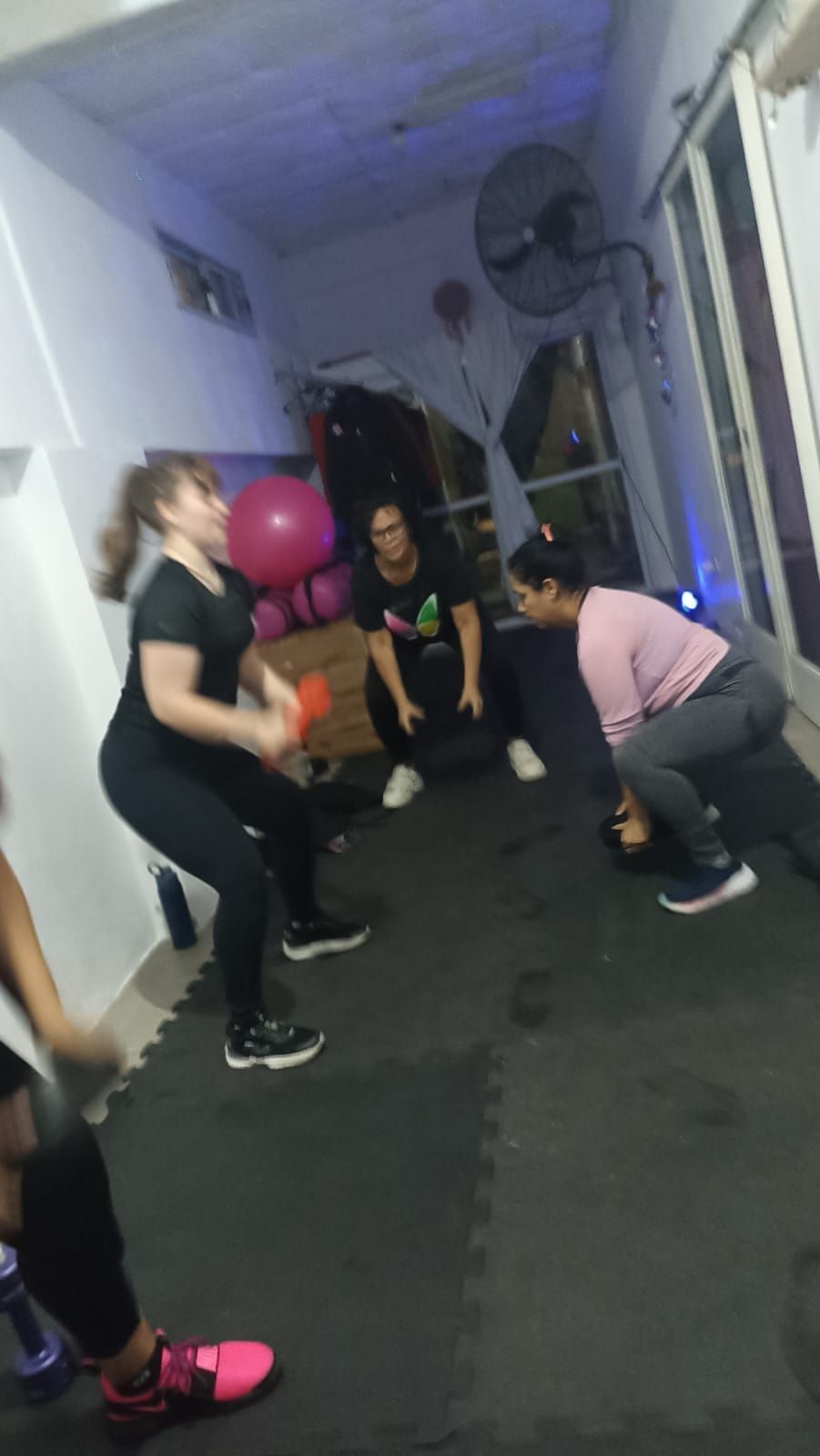 Personas haciendo ejercicio con pesas en un gimnasio. Una mujer vestida de negro hace sentadillas con una pelota.