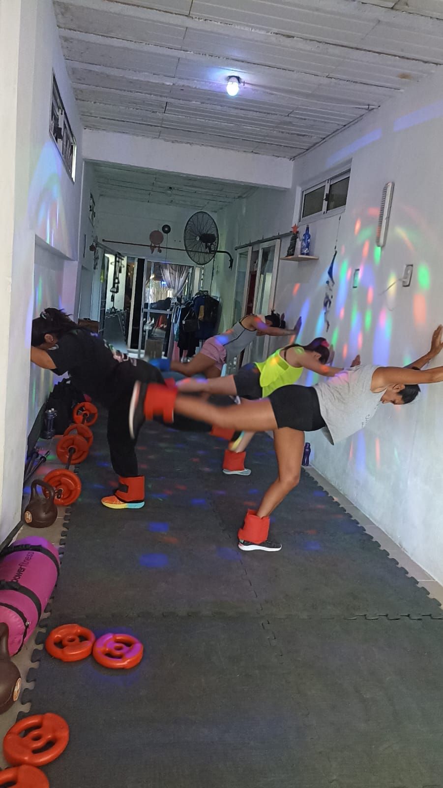 Personas en un gimnasio practicando una patada lateral apoyados en la pared.