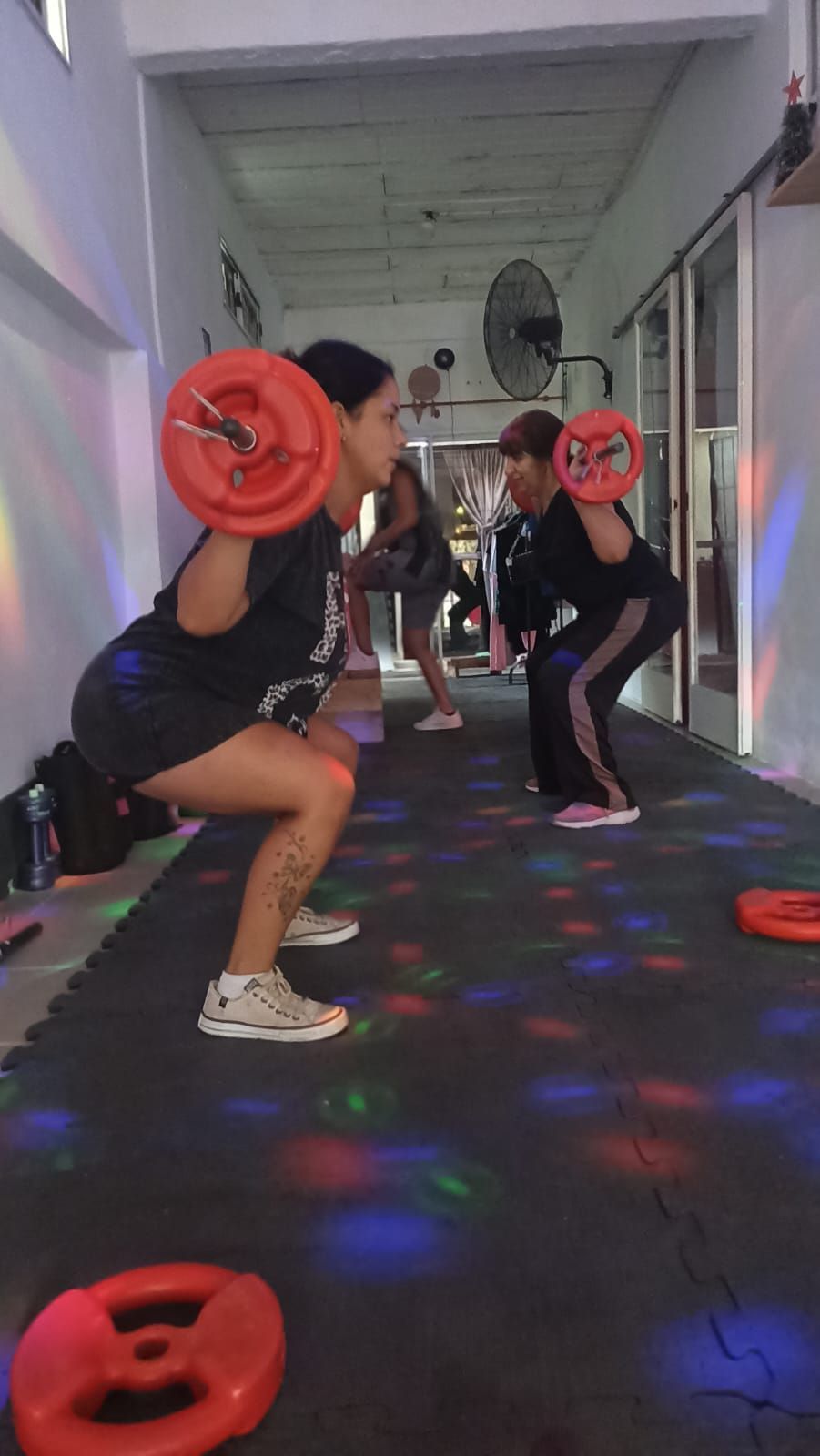Personas haciendo sentadillas con pesas en un gimnasio con luces de colores.