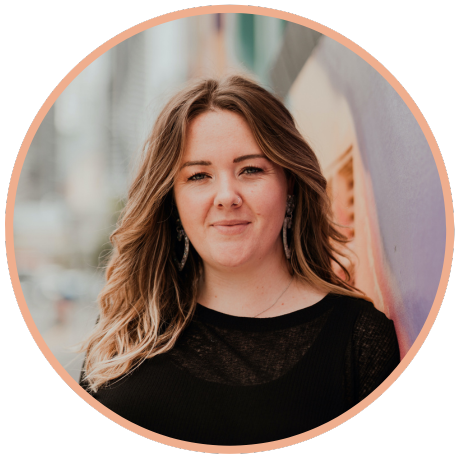 Portrait of a person with wavy, light-brown hair and dangling earrings, smiling softly against a blurred, colorful wall.