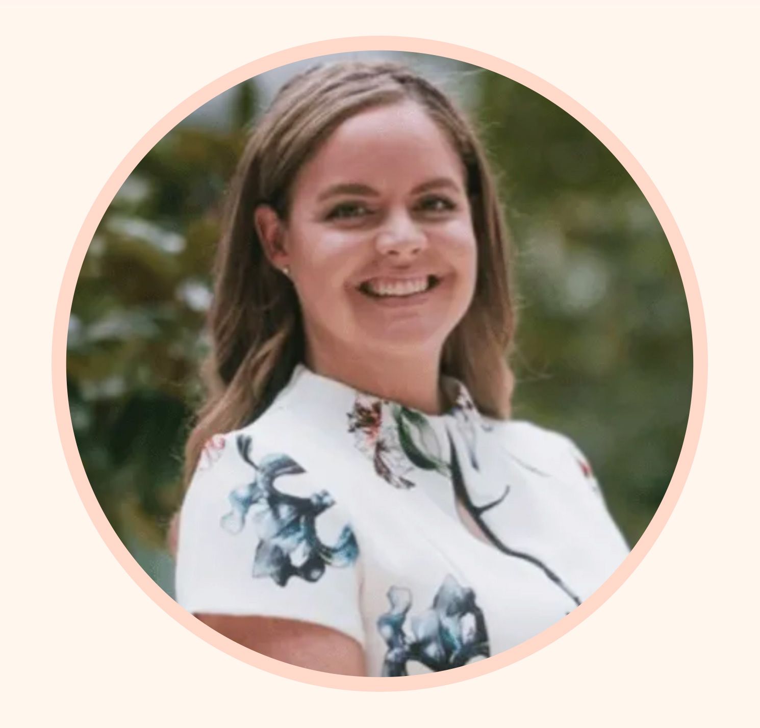 A smiling person wearing a floral print top in a circular frame against a soft, blurred background.
