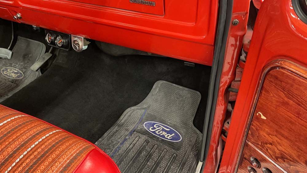 The interior of a red ford truck with a ford logo on the floor mat.