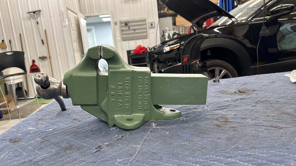 A green vise is sitting on top of a blue table in a garage.