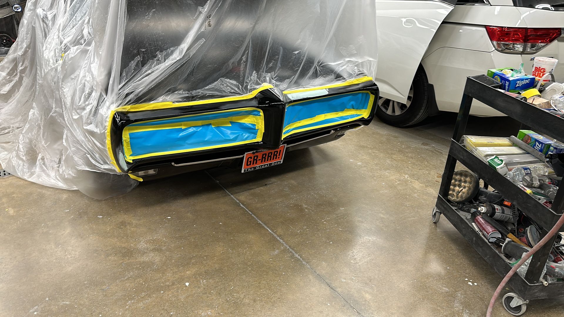 A car is covered in plastic while being painted in a garage.