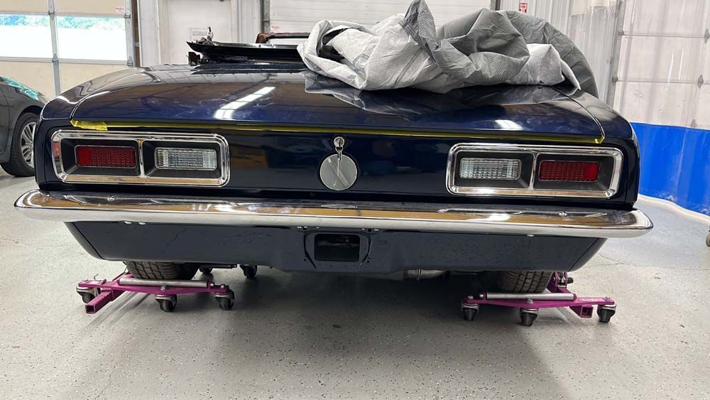 A blue car is sitting on a pink jack in a garage.