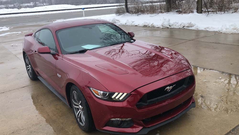 A red ford mustang is parked in a driveway in the snow.