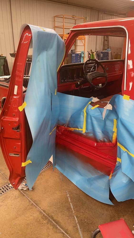 A red truck is being painted in a garage with the door open.