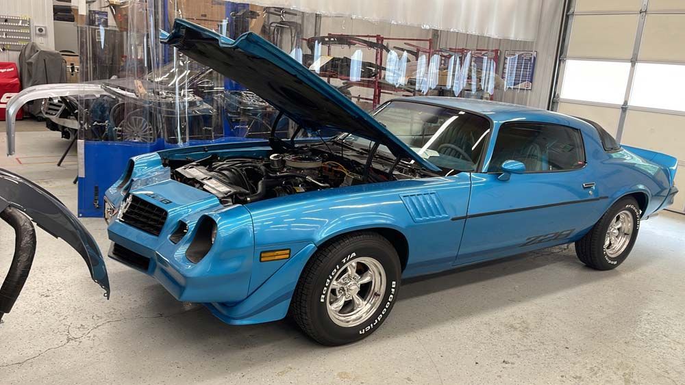 A blue car with the hood up is parked in a garage.