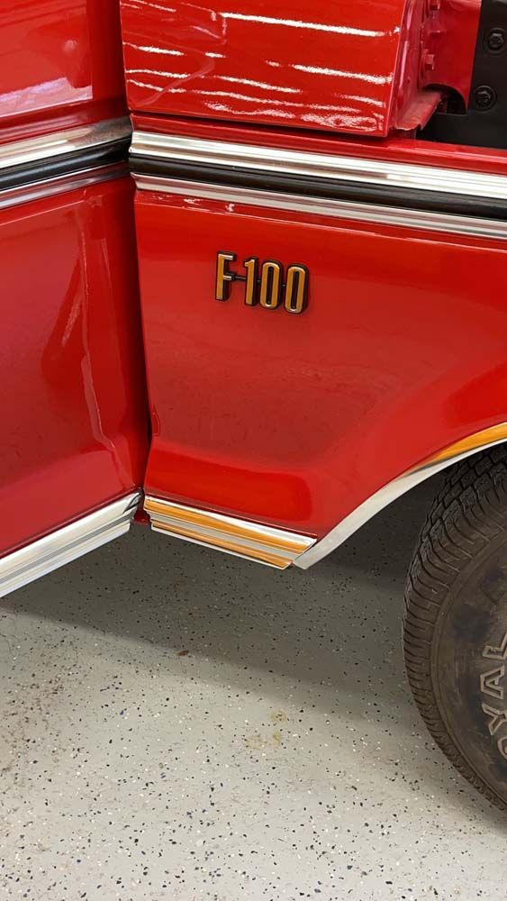 A red ford f100 truck is parked in a garage with the door open.