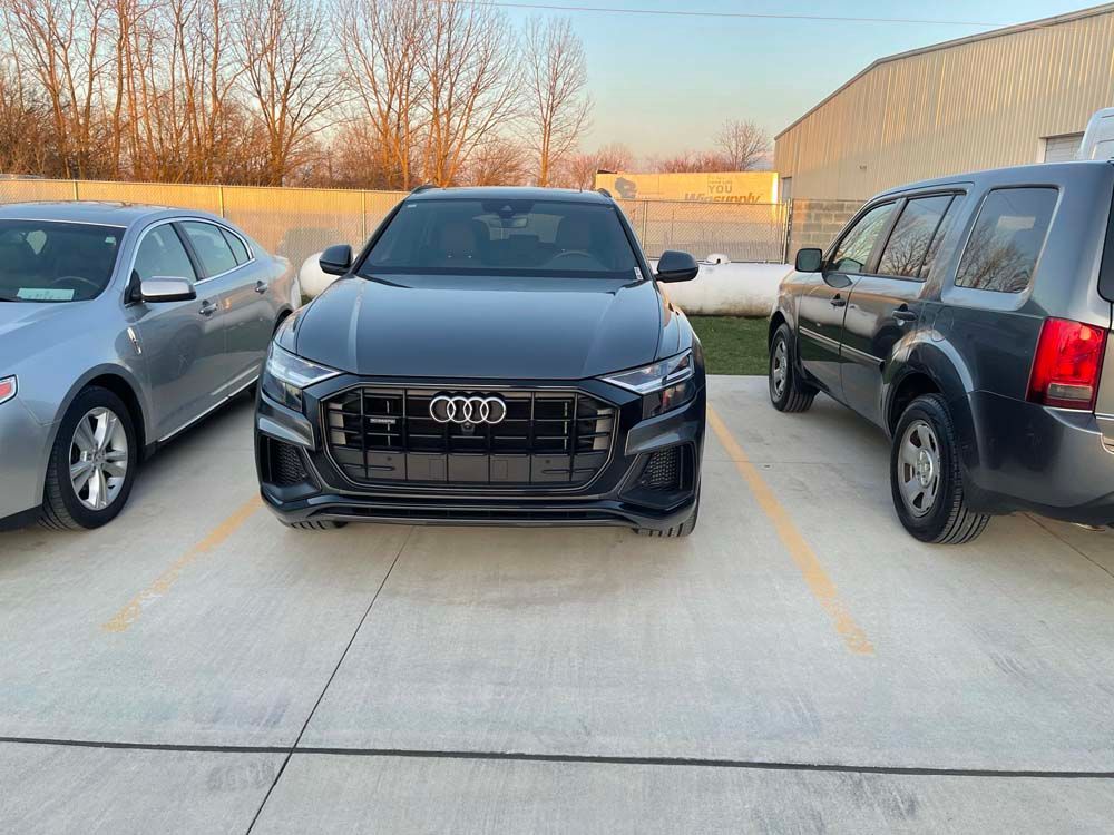 A black audi q8 is parked in a parking lot next to other cars.