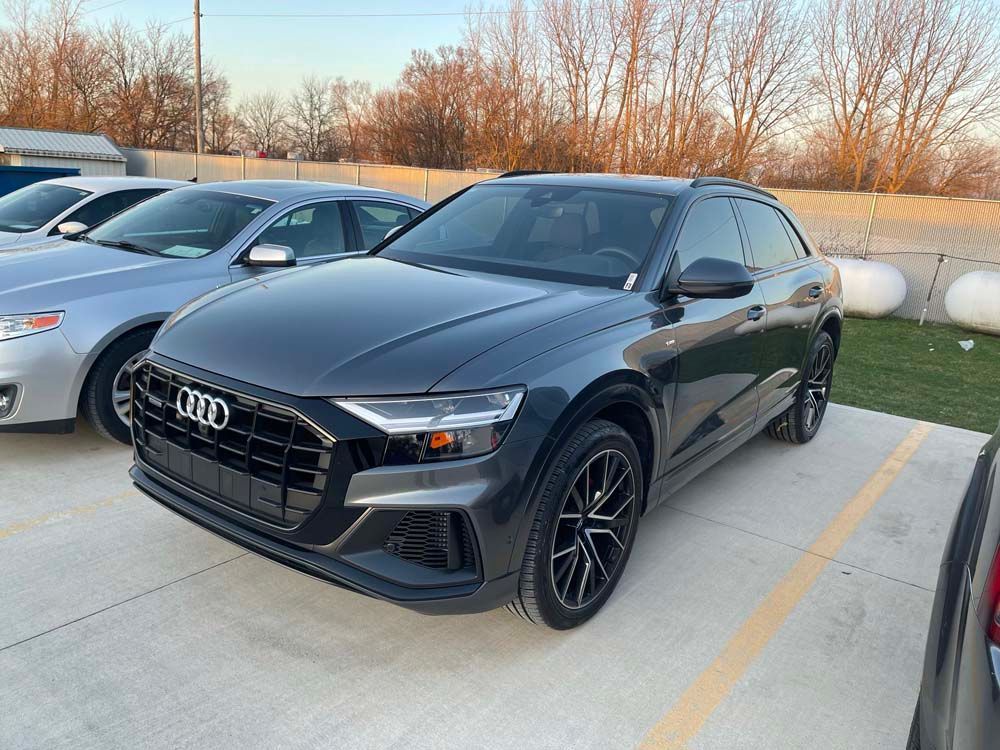 A black audi q8 is parked in a parking lot next to other cars.