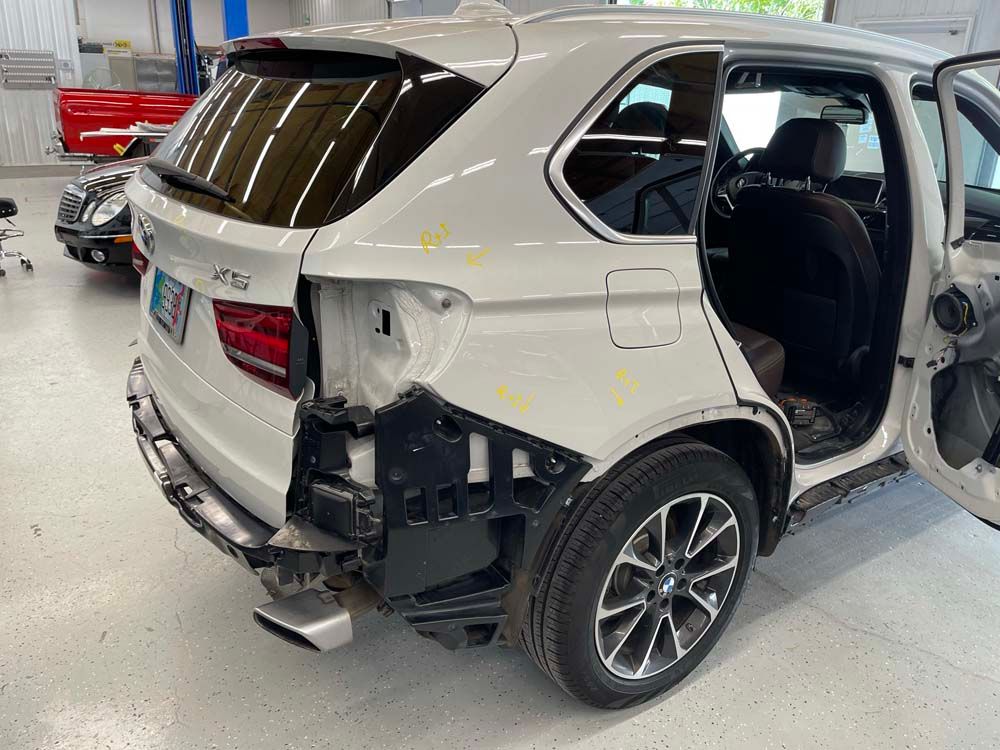 A white bmw x5 is being repaired in a garage.