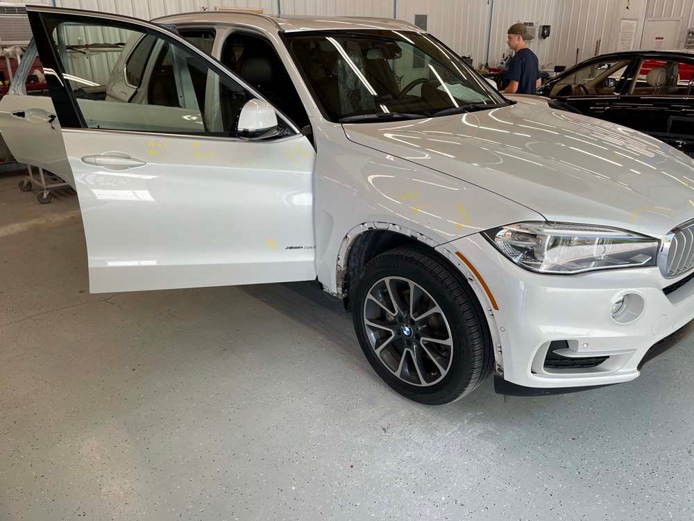 A white bmw x5 is parked in a garage with its doors open.