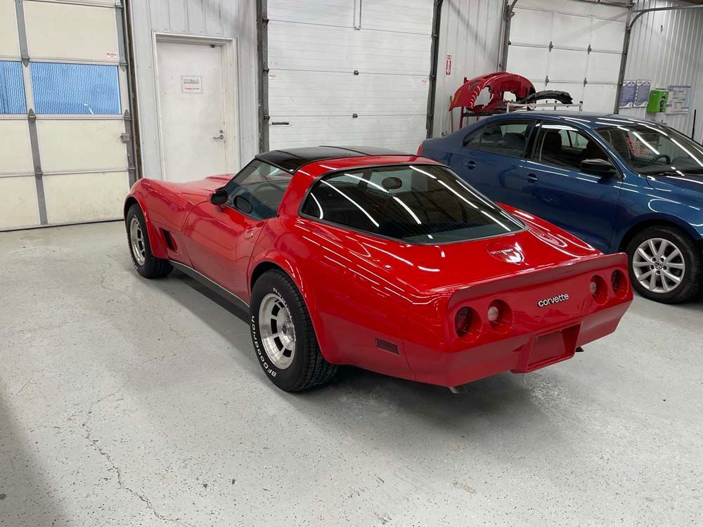 A red corvette is parked in a garage next to a blue car.
