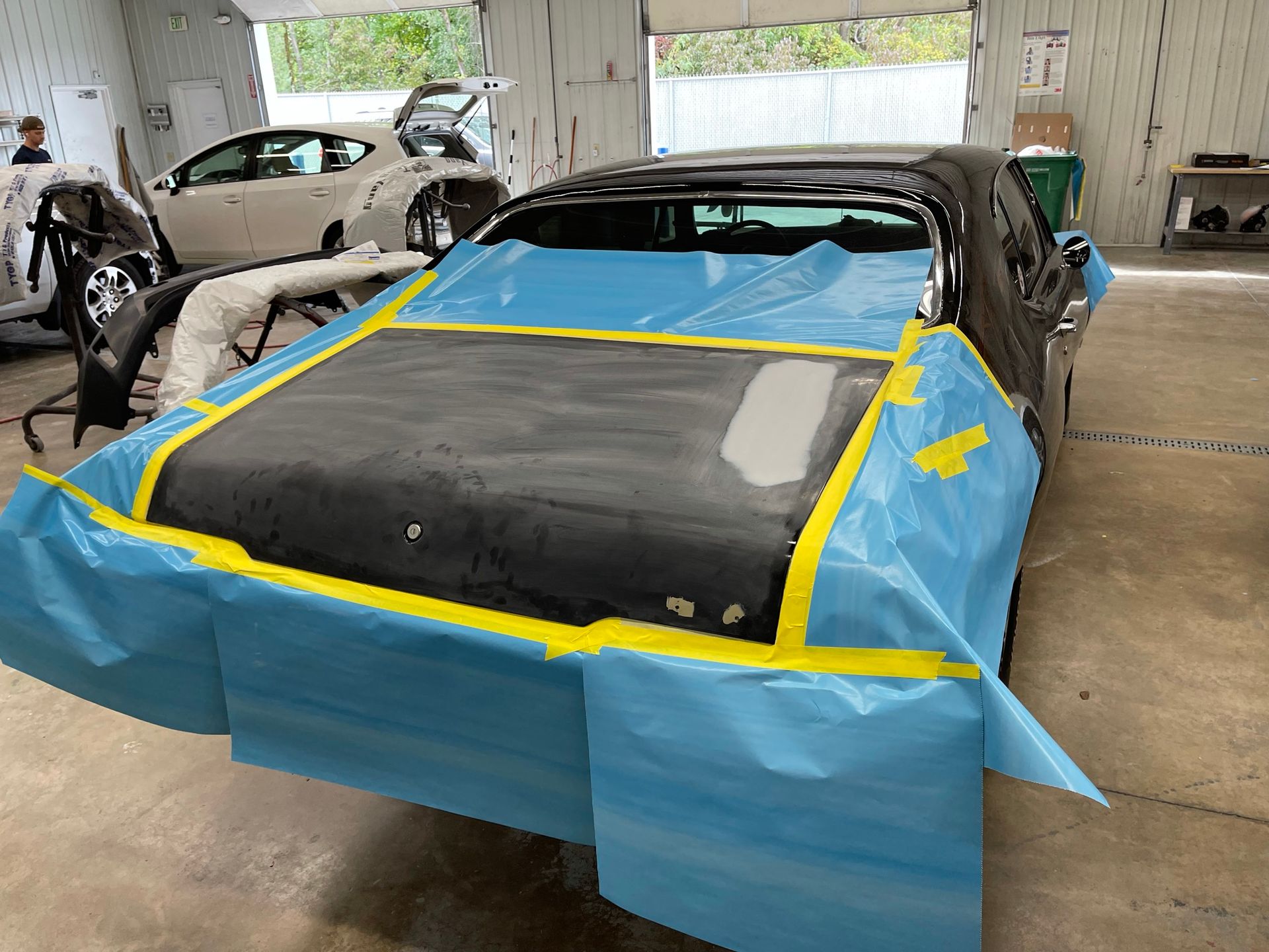 A car is covered in blue plastic and tape in a garage.