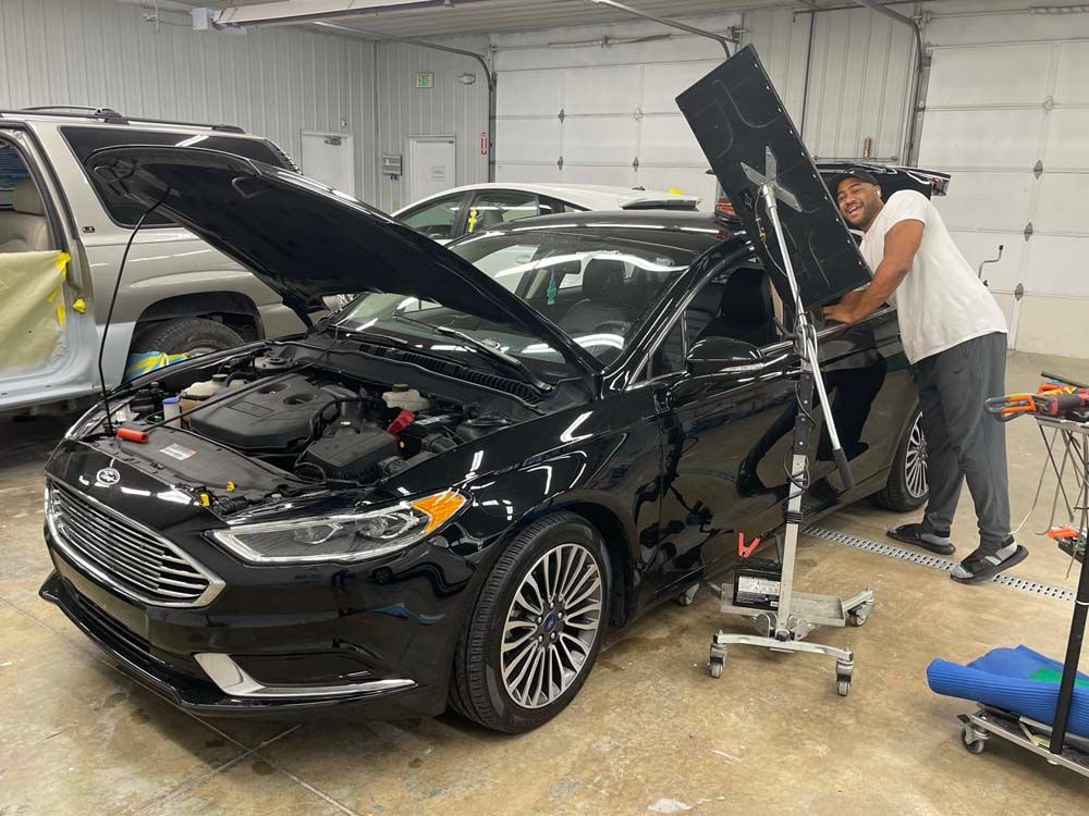 A man is working on a black car in a garage with the hood up.