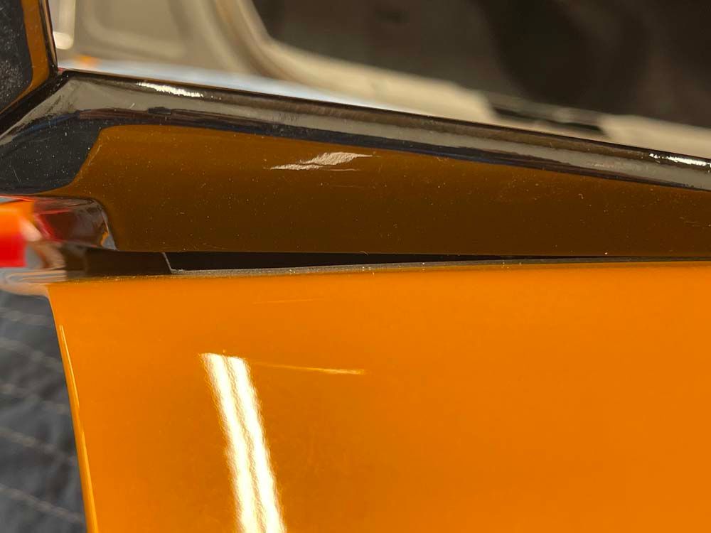 A close up of the side of an orange car with a chrome trim.