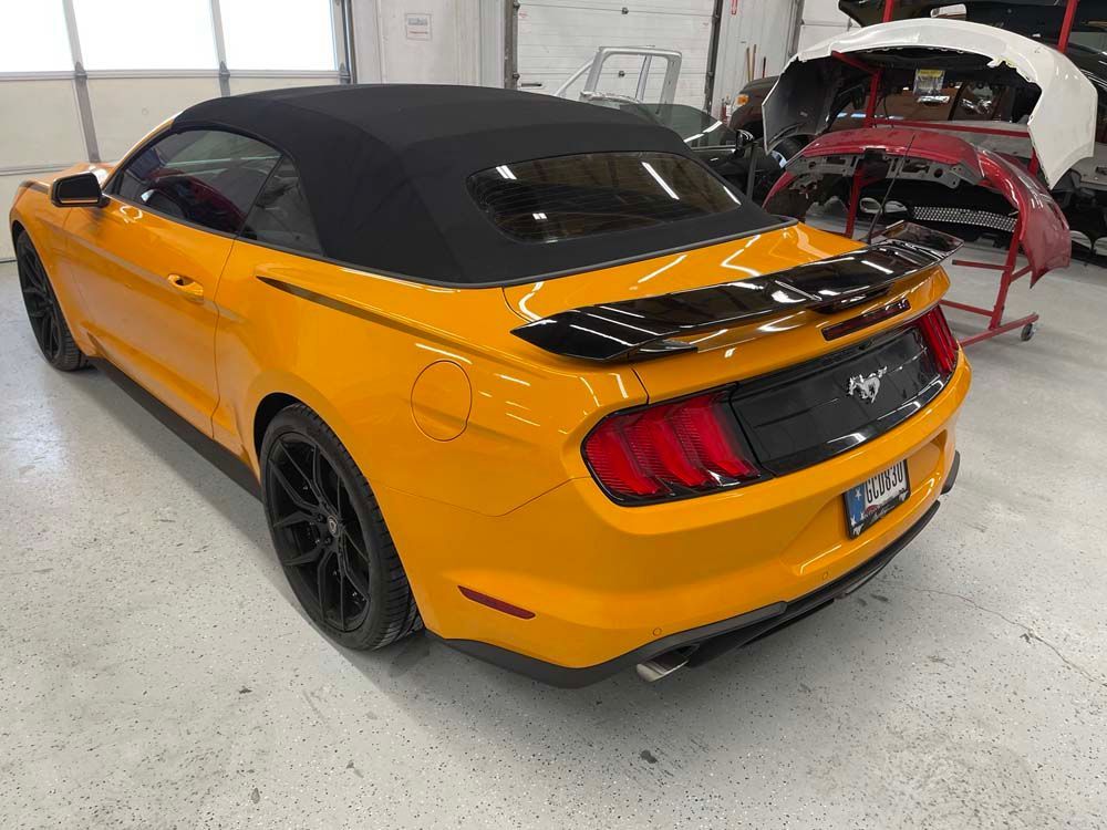 A yellow mustang convertible is parked in a garage.