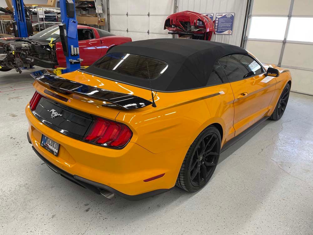 A yellow mustang convertible is parked in a garage.